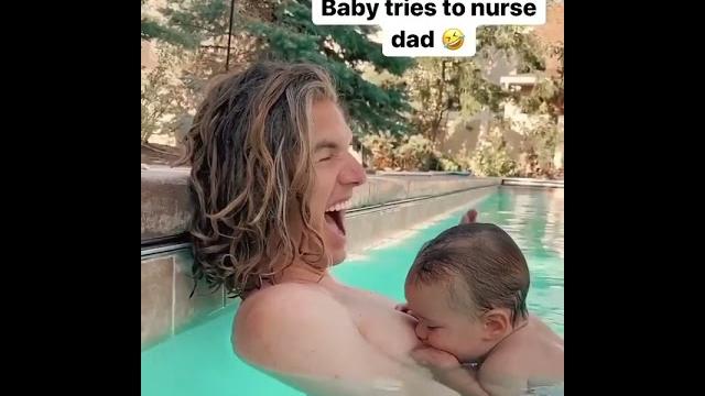 The baby tries drinking milk from his dad. The baby tries drinking milk from his dad.