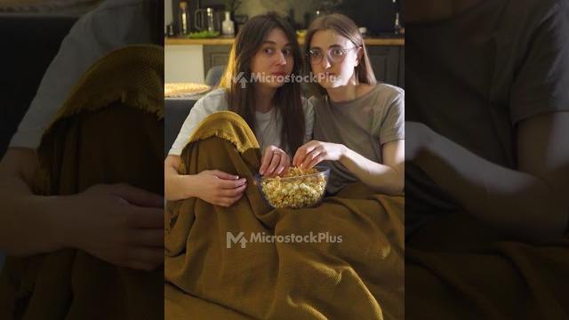 Girlfriends shocked by tv show. women with frightened face sitting on couch late at night watching Girlfriends shocked by tv show. women with frightened face sitting on couch late at night watching